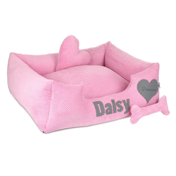 Daisy – legowisko dla psa z dekoracjami i miękkim wnętrzem Różowe legowisko dla psa z wyjmowaną poduszką i ozdobami: kostką i sercem z napisem „Princess”, imię „Daisy” wyszyte z przodu.